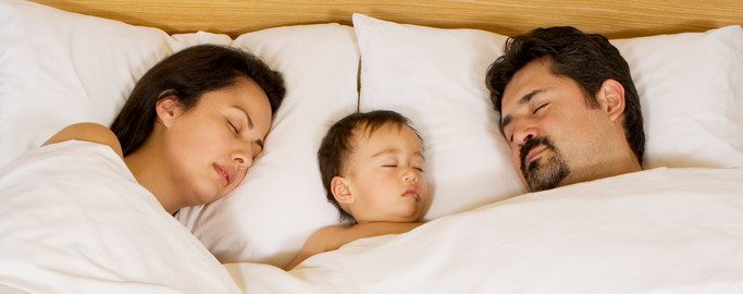 Parents Lying with Infant in Bed --- Image by © MM Productions/Corbis