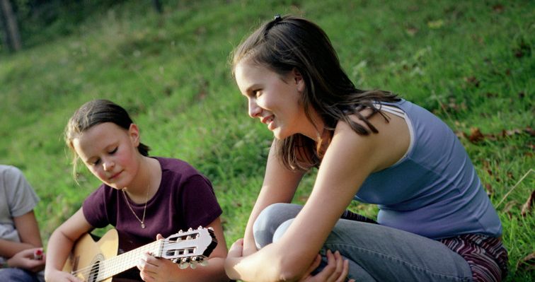 Three Girls Sitting with Guitar in Meadow --- Image by © Mika/Corbis